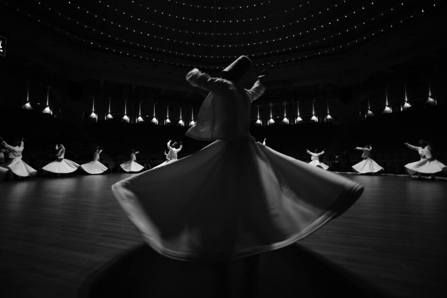 Whirling dervishes dancing on stage in traditional Sufi attire under dramatic lighting