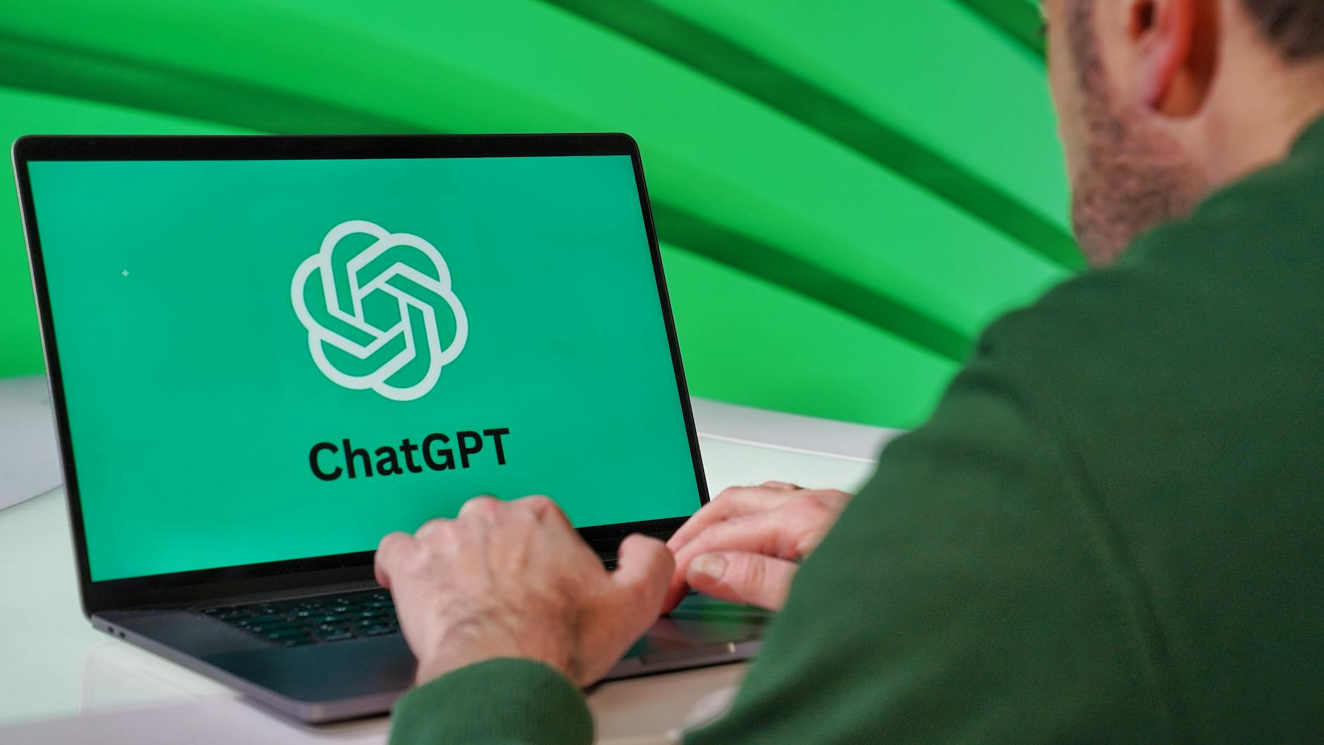 man using chatgpt on laptop with green background