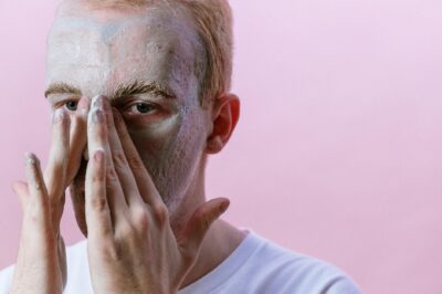 A man in a white crew-neck shirt covering his face, representing sensitive or irritated skin.
