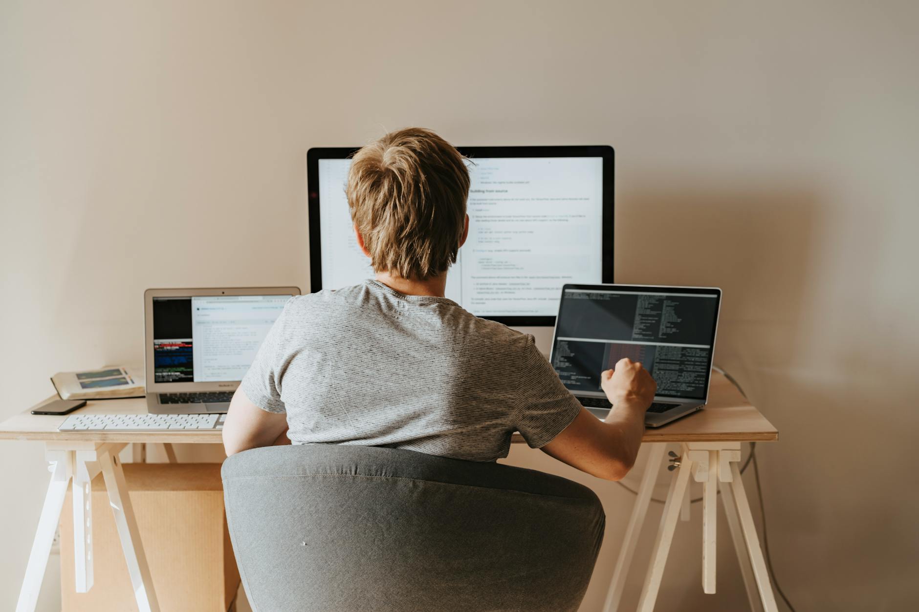 back view of a boy sitting on grey chair while using his laptop computers