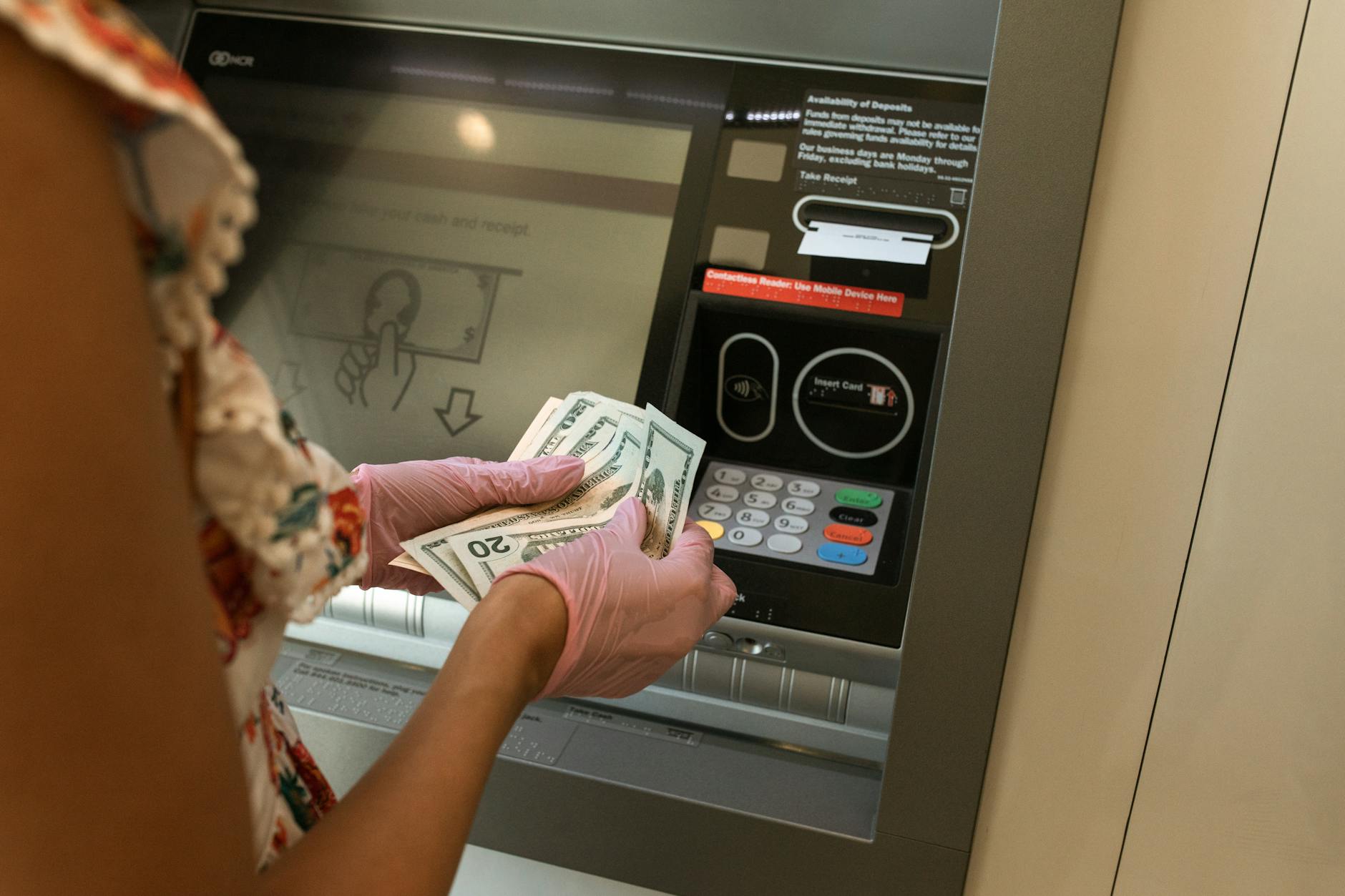 person counting money in front of atm